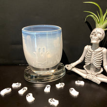 Load image into Gallery viewer, And etched ghost botive is on display with small white acrylic ghost table scatter. Sitting next to the votive is a skeleton sculpture in a yoga pose with an air plant as hair.

