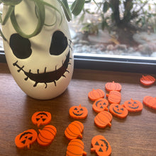 Load image into Gallery viewer, Orange acrylic pumpkins are shown on a wooden windowsill with a small white planter with a sugar skull face. Some rockery is in the background. 
